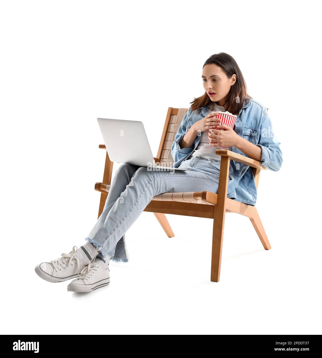 Shocked young woman with popcorn and laptop watching video in armchair on white background Stock Photo