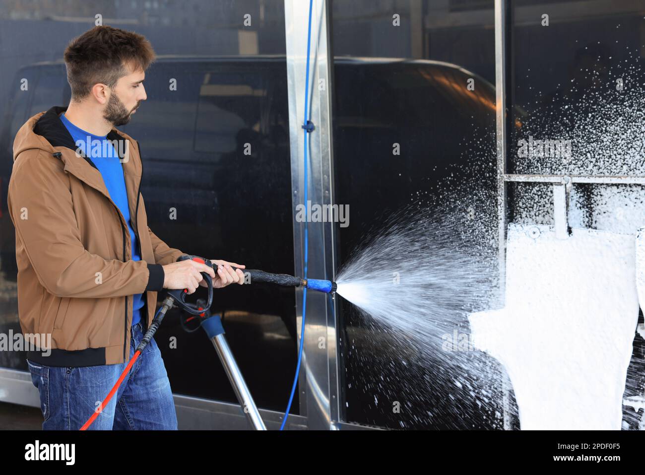 Man cleaning auto mats with high pressure foam jet at selfservice car