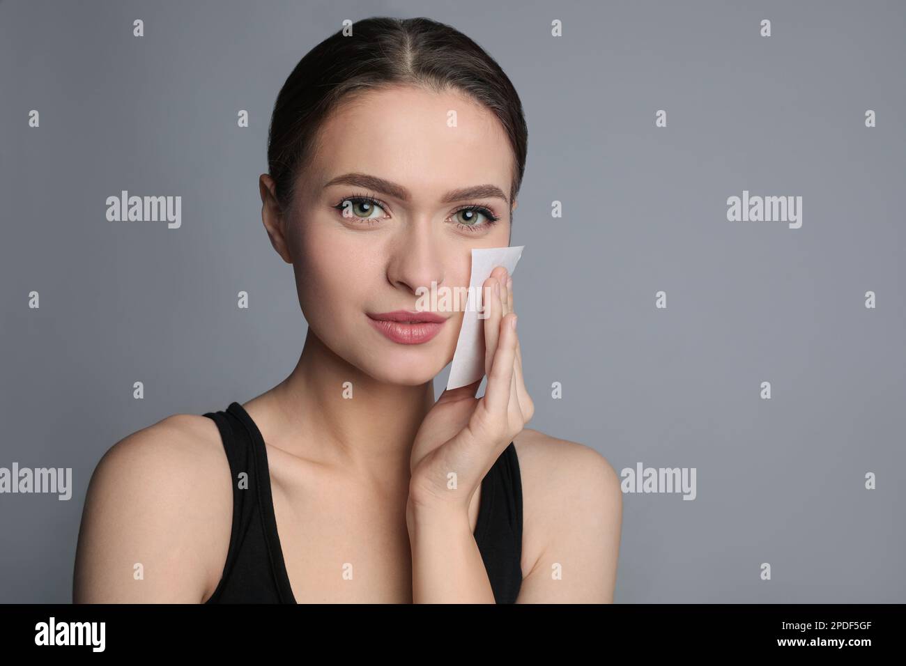 Beautiful woman using mattifying wipe on grey background Stock Photo
