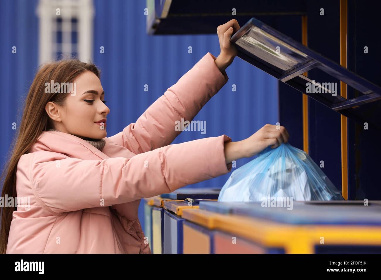 Woman throwing garbage into bin at recycling point outdoors Stock Photo