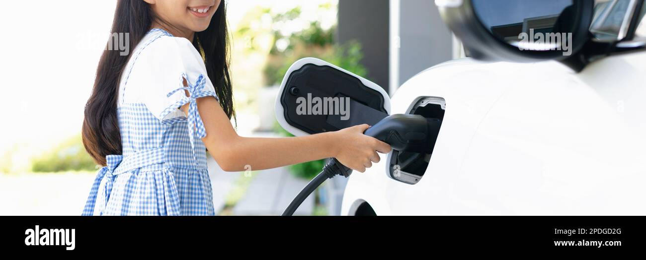 A playful girl holding an EV plug, a home charging station providing a