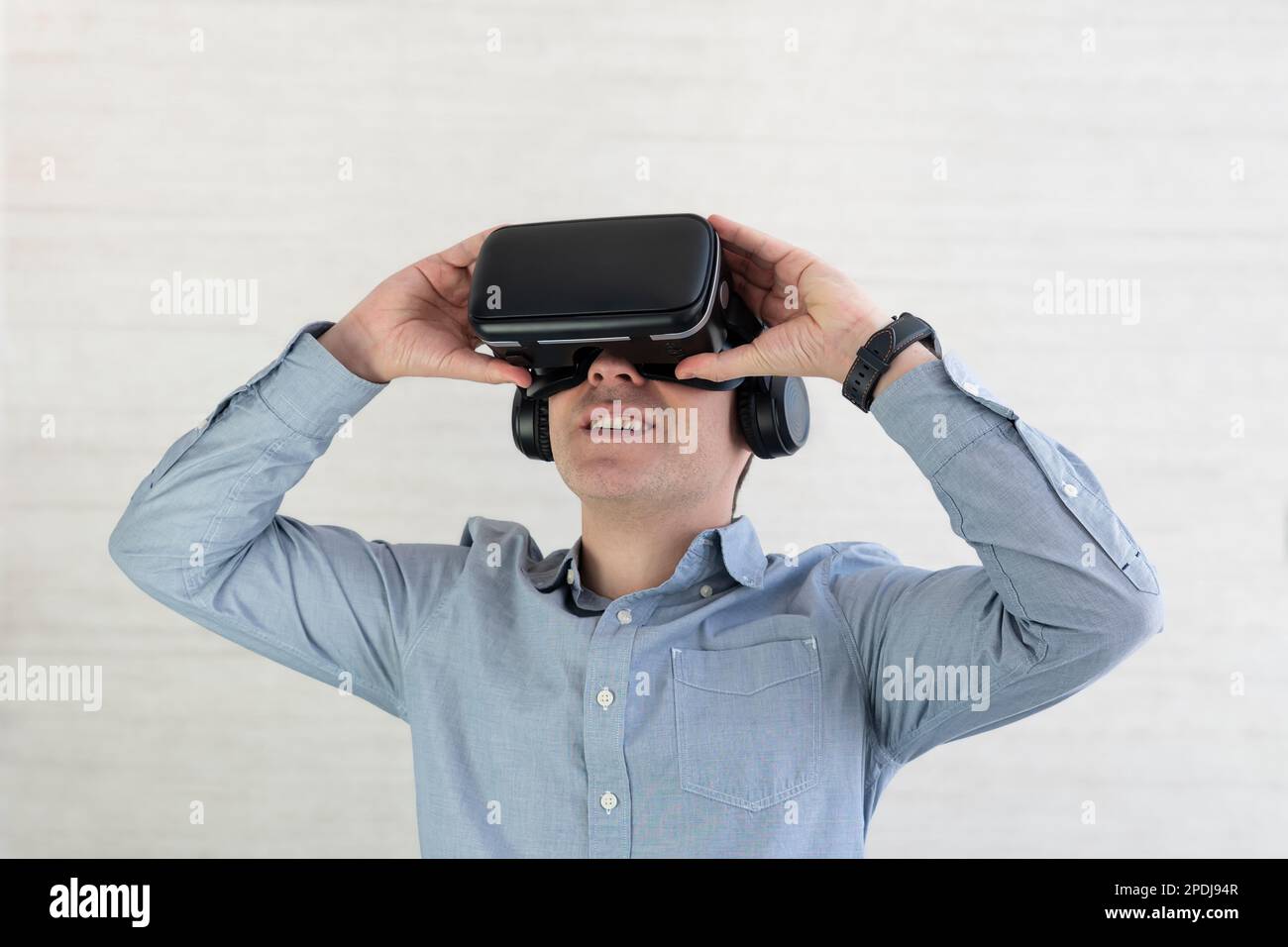 Young guy in casual using VR glasses, touching something invisible at copy space, millennial man experiencing virtual reality adventure on grey backgr Stock Photo