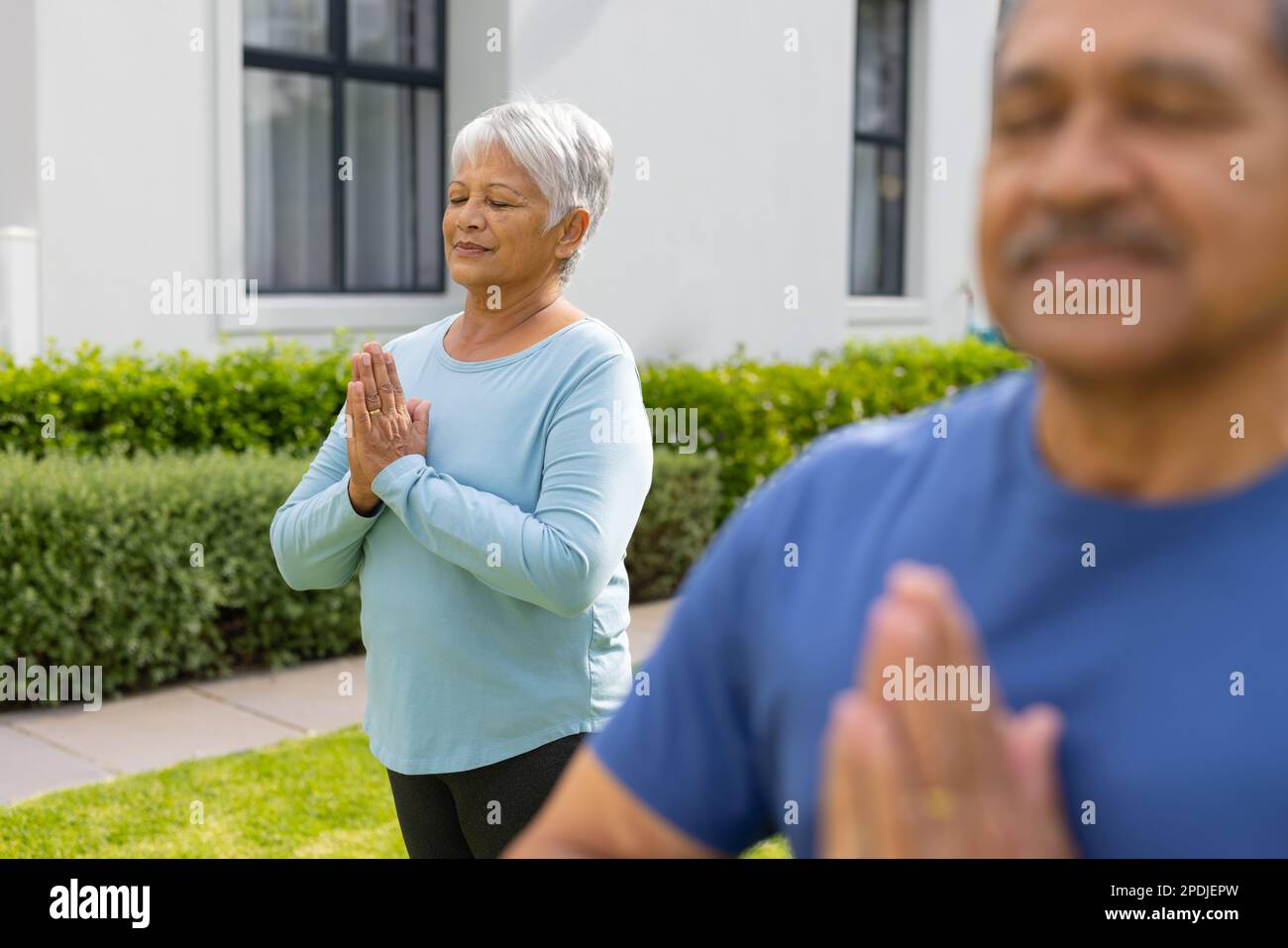 Biracial senior woman and man meditating in prayer pose against house at yard Stock Photo