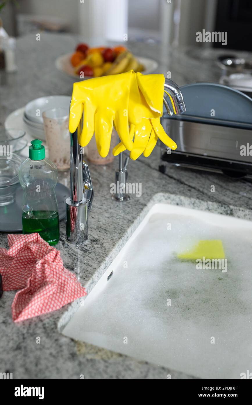 Soap dispenser by yellow washing up gloves on faucet and kitchen sink
