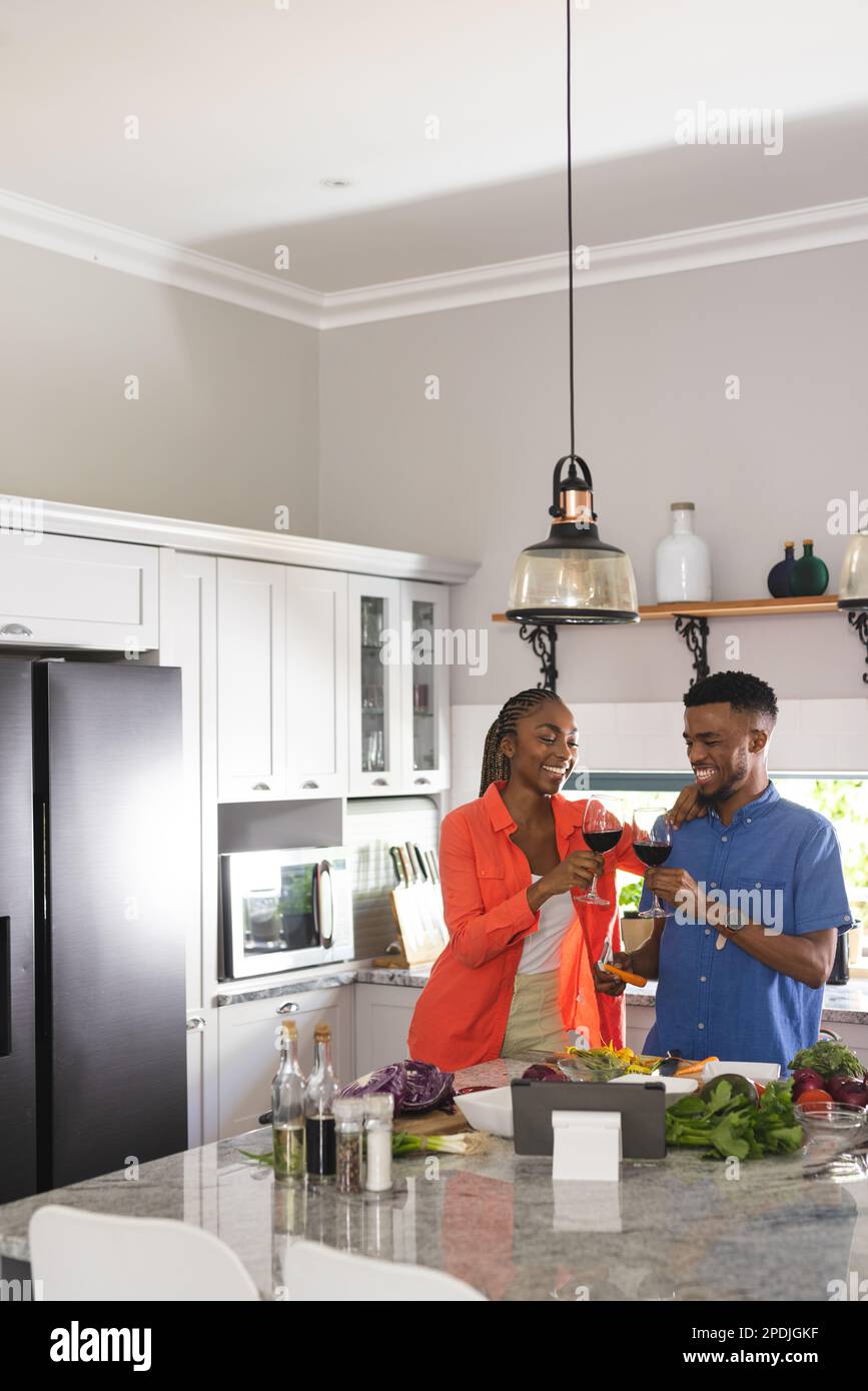 Happy african american couple cooking dinner together, drinking red ...