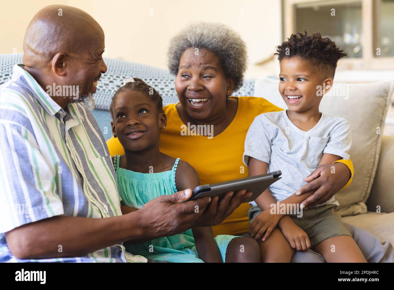 Happy african american grandparents and grandchildren sitting on sofa and using tablet Stock Photo