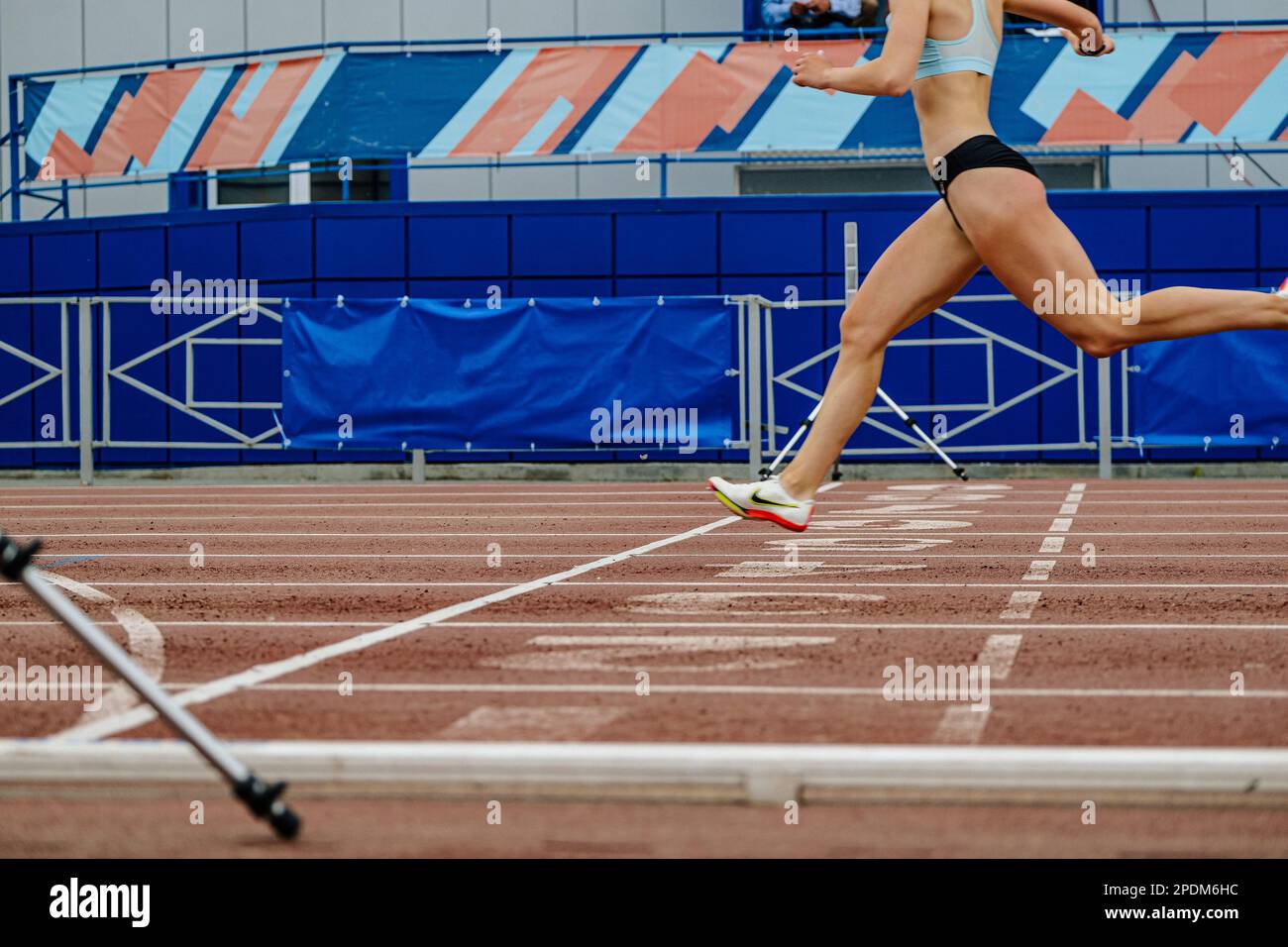 female runner crosses finish line of 100-meter race in athletics competition, Nike spikes shoes, summer sports games Stock Photo