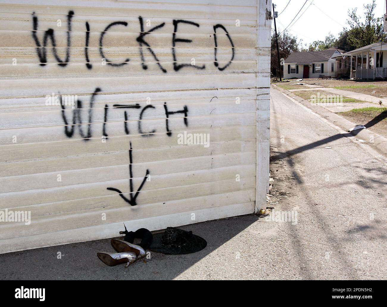 Leggings, silver shoes and a witch hat sit under a Wicked Witch sign  painted on a house in the middle of a suburban street while another house  sits off its' foundation in
