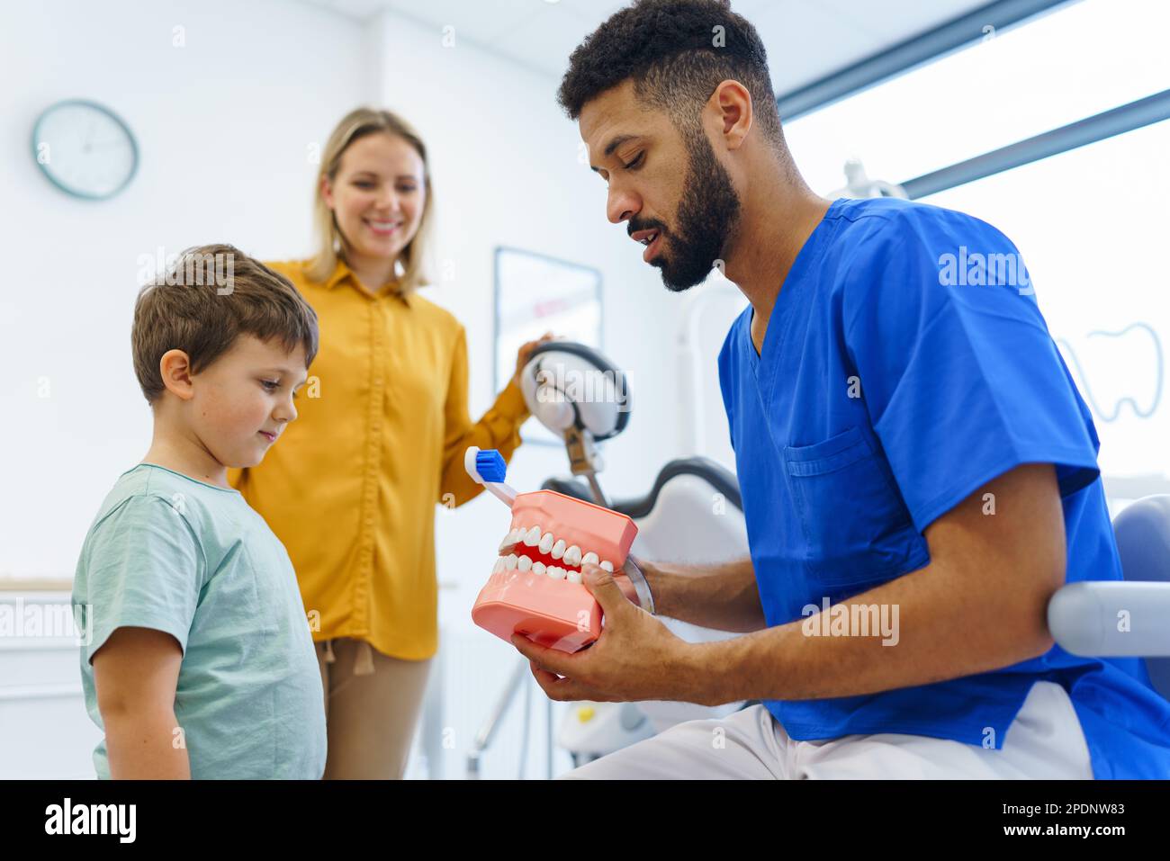 Young multiracial dentist showing little boy how to clean teeth
