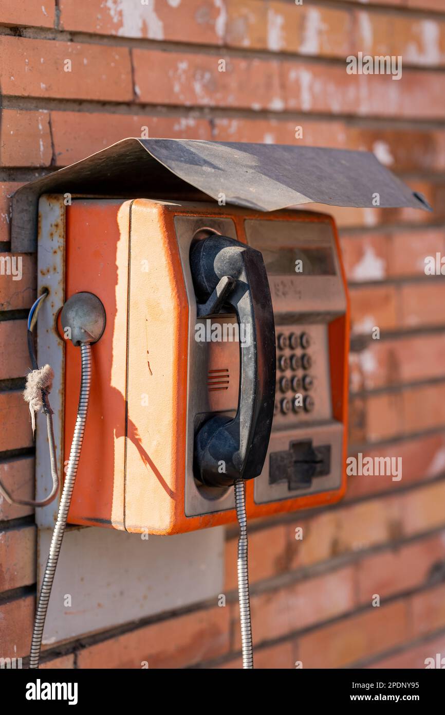 A vintage public telephone mounted on a brick wall, displaying a retro aesthetic Stock Photo