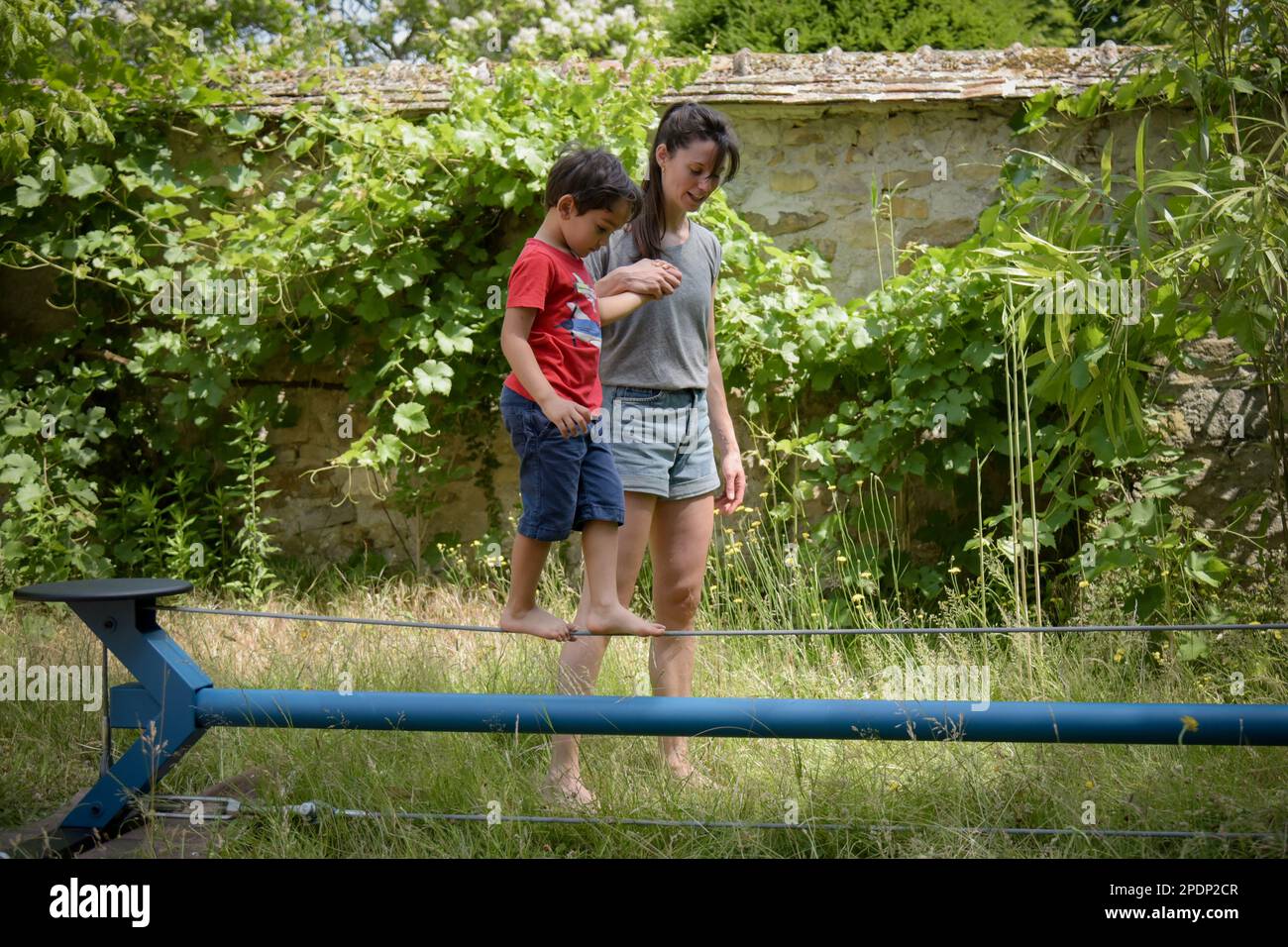 young boy walking on a wire with the help of a woman coach in a garden Stock Photo