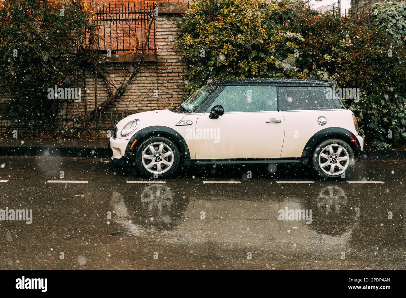 Side View Of beige white Color Mini Cooper S Car Parked On Street near old house. Stock Photo