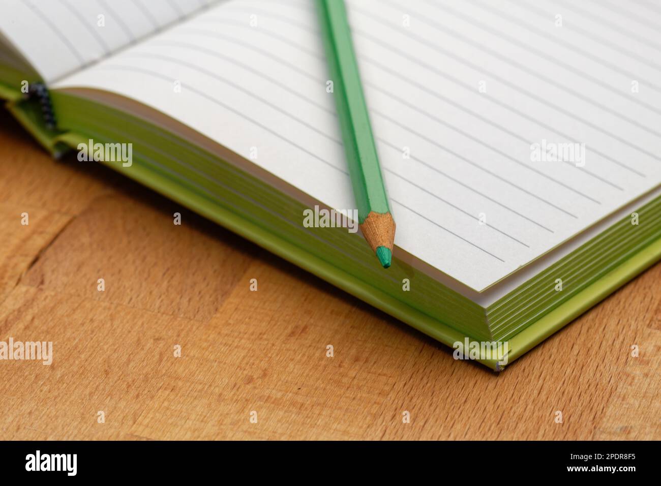 A lined notebook with a green pencil. Ready to take notes, sketch ideas and write plans. Pencil and paper at the ready. Stock Photo