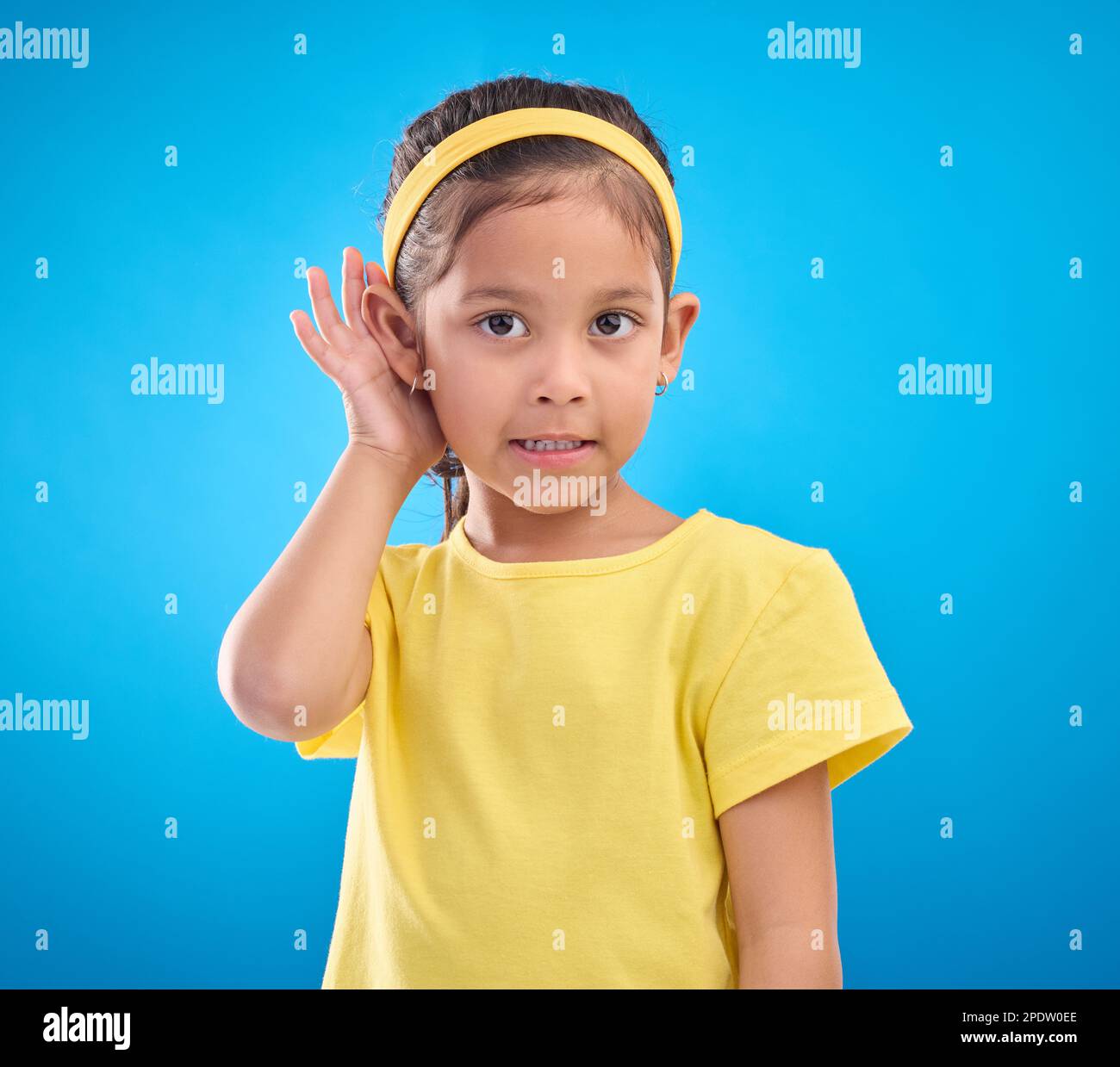 Hearing, eavesdrop and portrait of a children listening isolated on a blue background in a studio. Listen, attention and young girl holding an ear for Stock Photo
