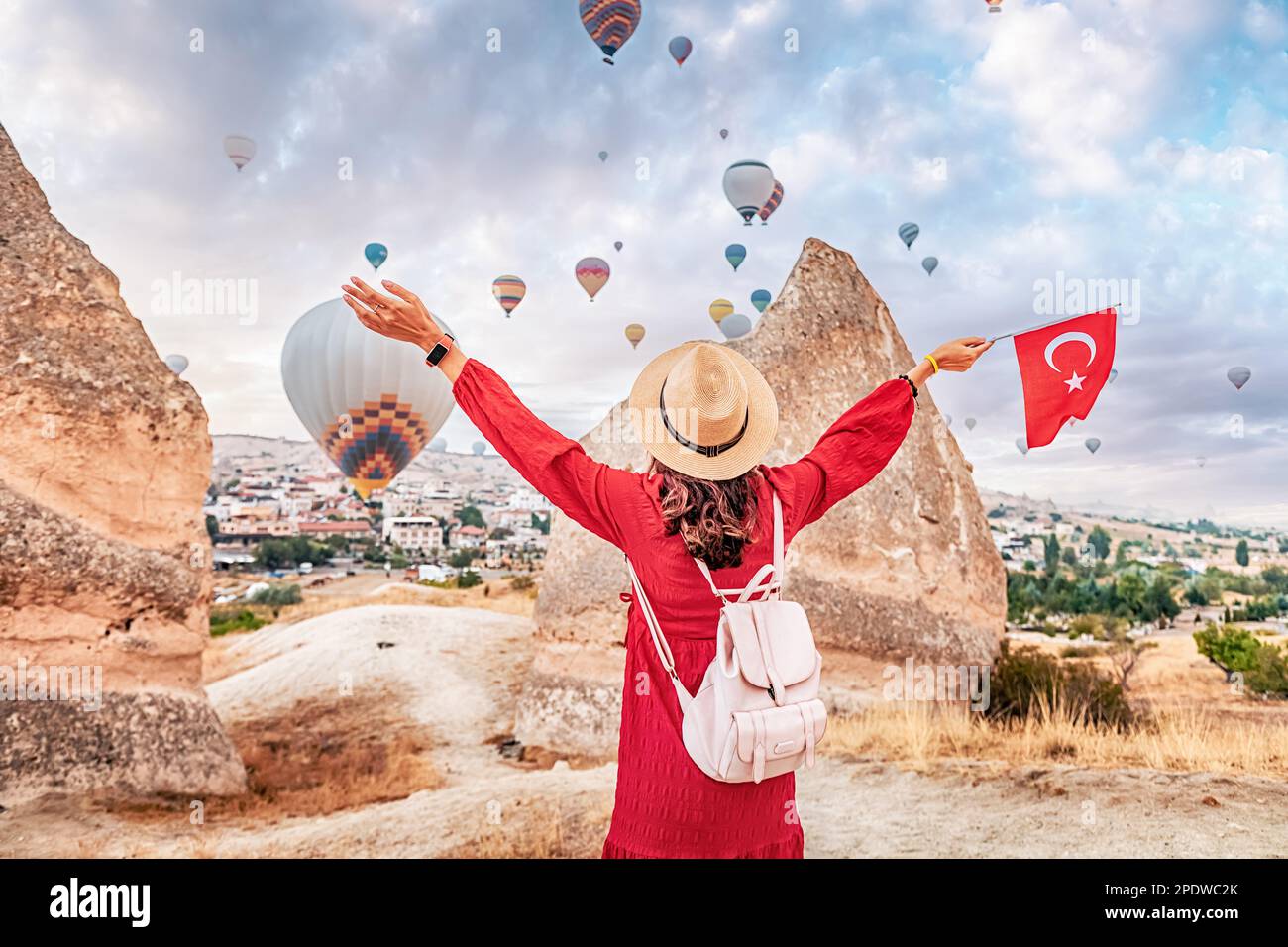 Take in the breathtaking views of Cappadocia, Turkey with a young woman as she watches the iconic hot air balloons and proudly displays the Turkish fl Stock Photo