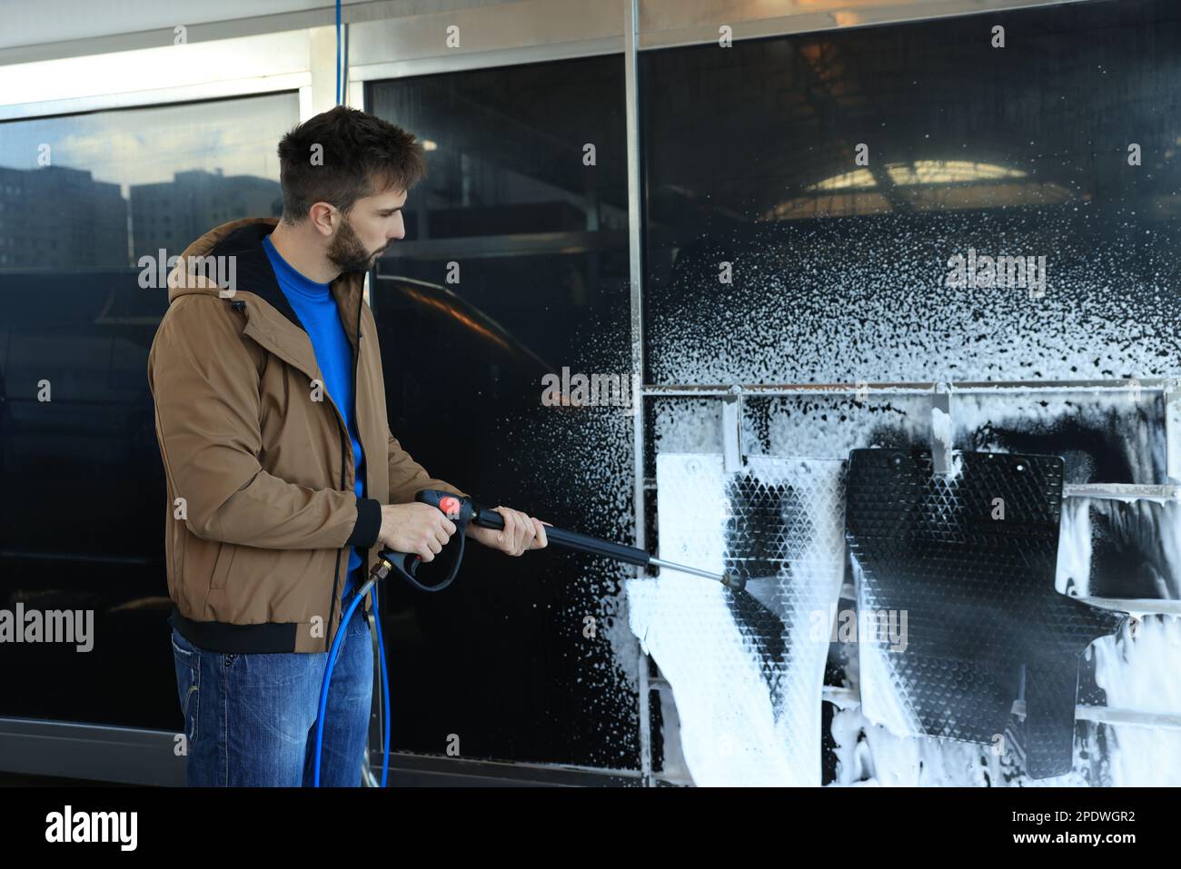 Man cleaning auto mats with high pressure water jet at selfservice car