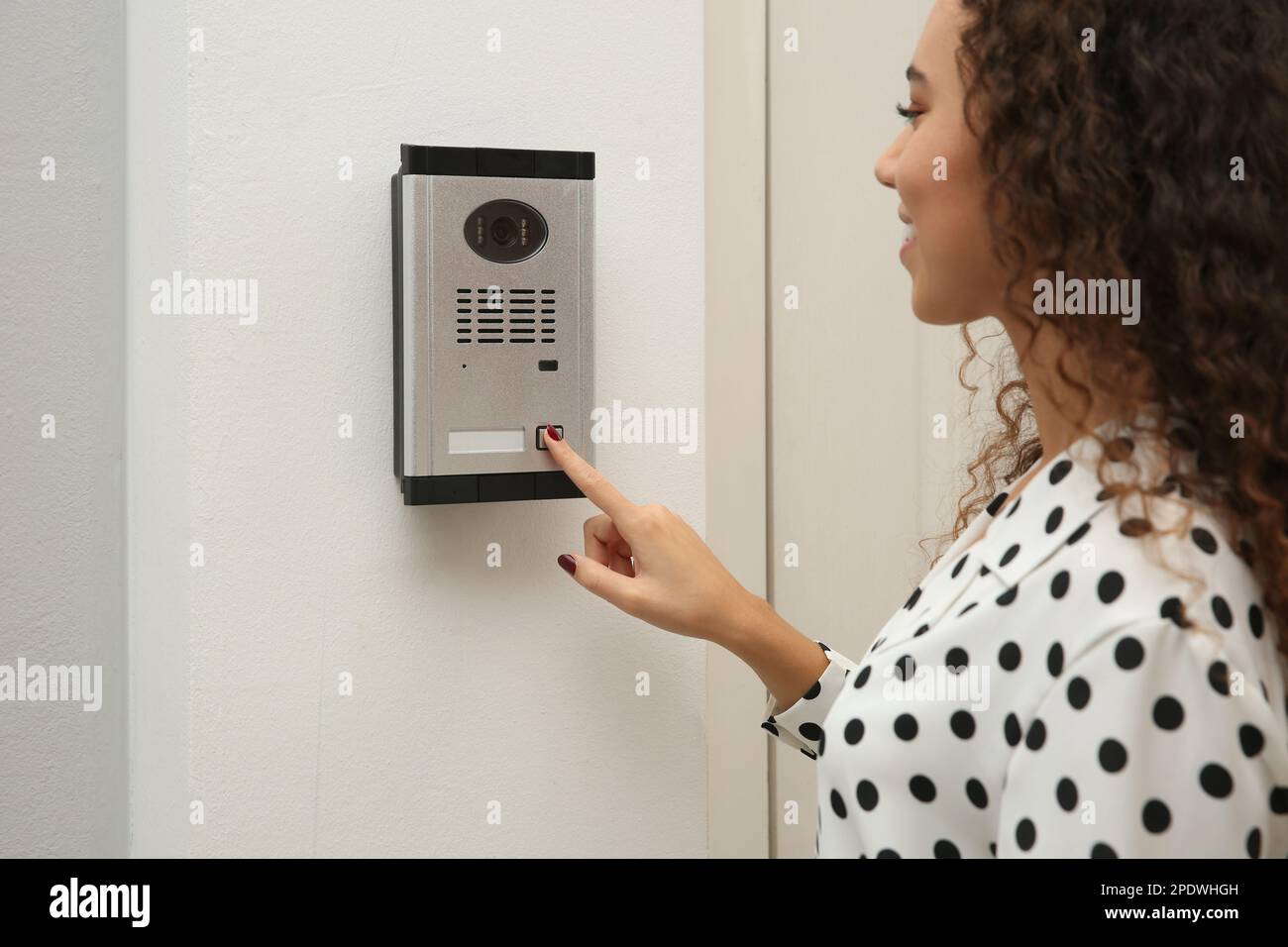 Young African-American woman ringing intercom with camera in entryway Stock Photo