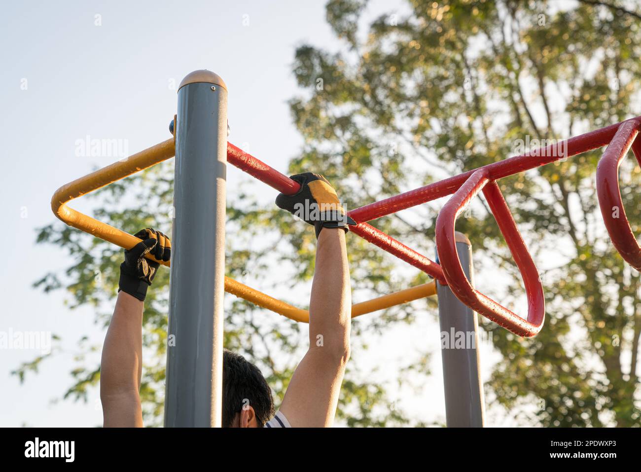 Man working out outdoors, arms swinging on monkey bar. Strength