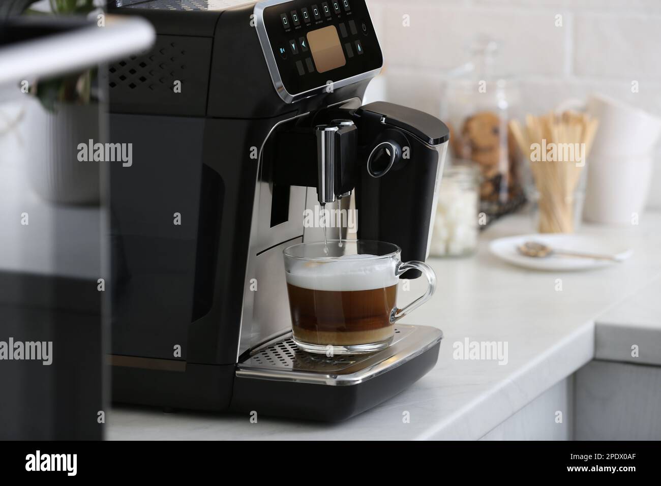 Modern electric espresso machine making coffee with milk on white marble countertop in kitchen