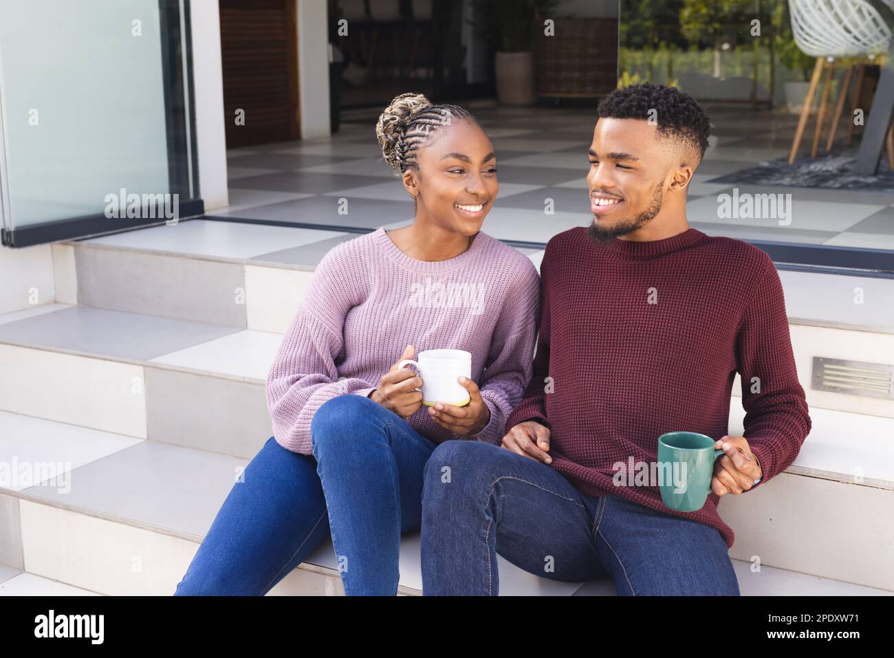 Happy african american couple sitting on stairs in garden, drinking ...