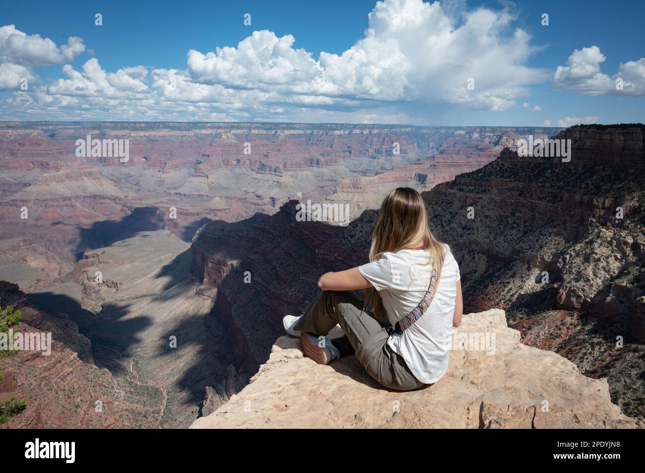 Long-haired blonde young girl sitting on the edge of the cliff of the ...