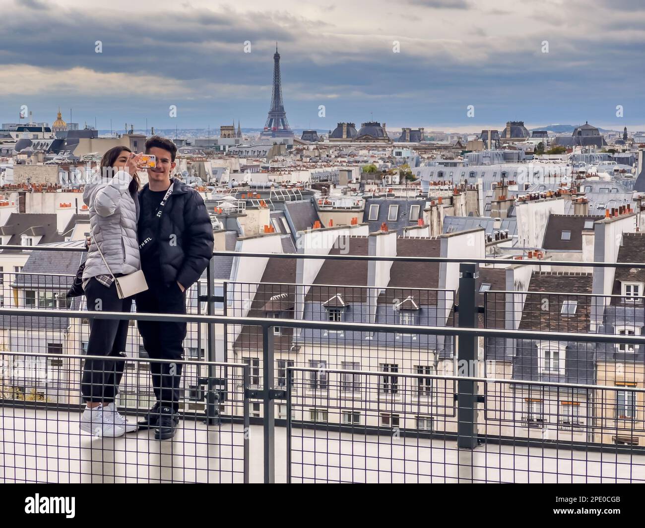 Paris France - 04.06.2022: Over the roof tops of Paris a young couple is taking a selfie with mobile phone with a beautiful genereal city view Stock Photo