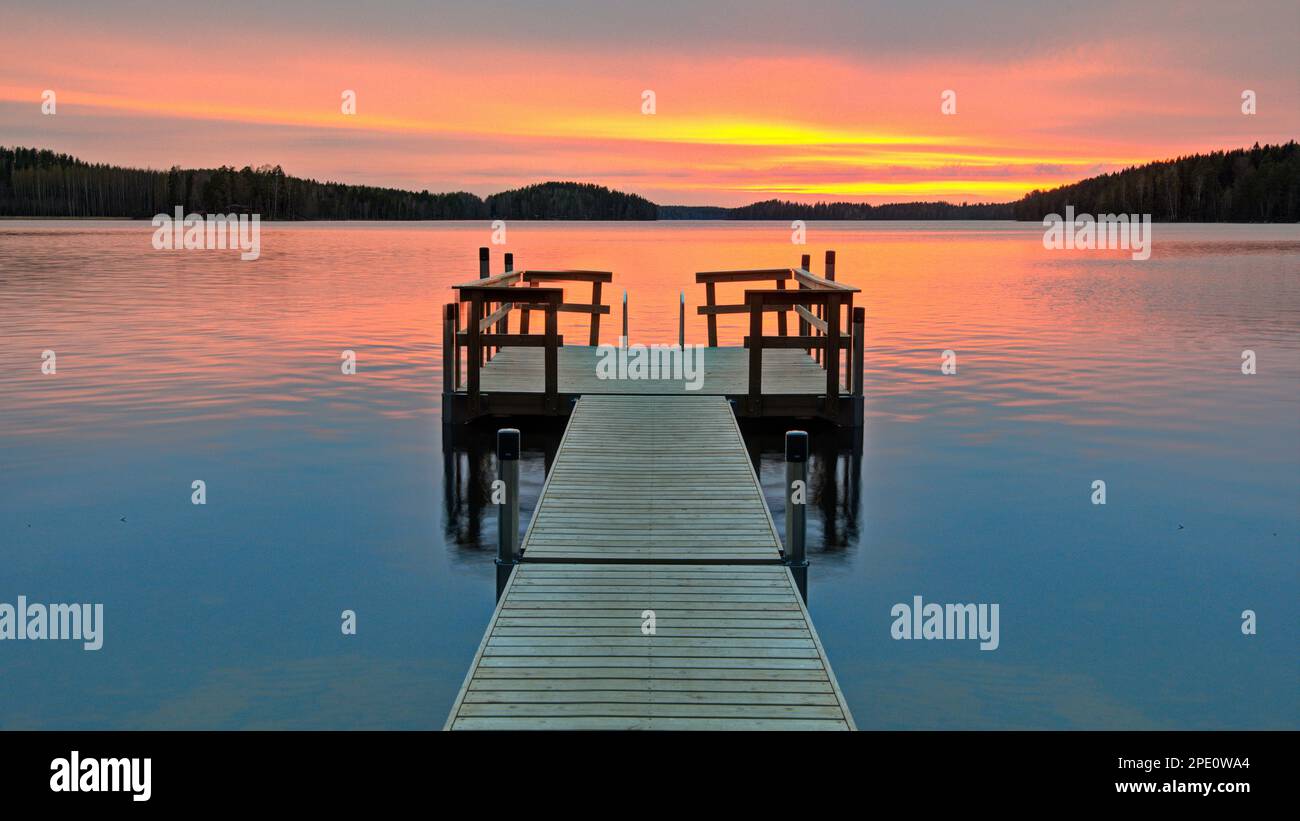 A wooden pier with a vibrant sunset sky in the background Stock Photo