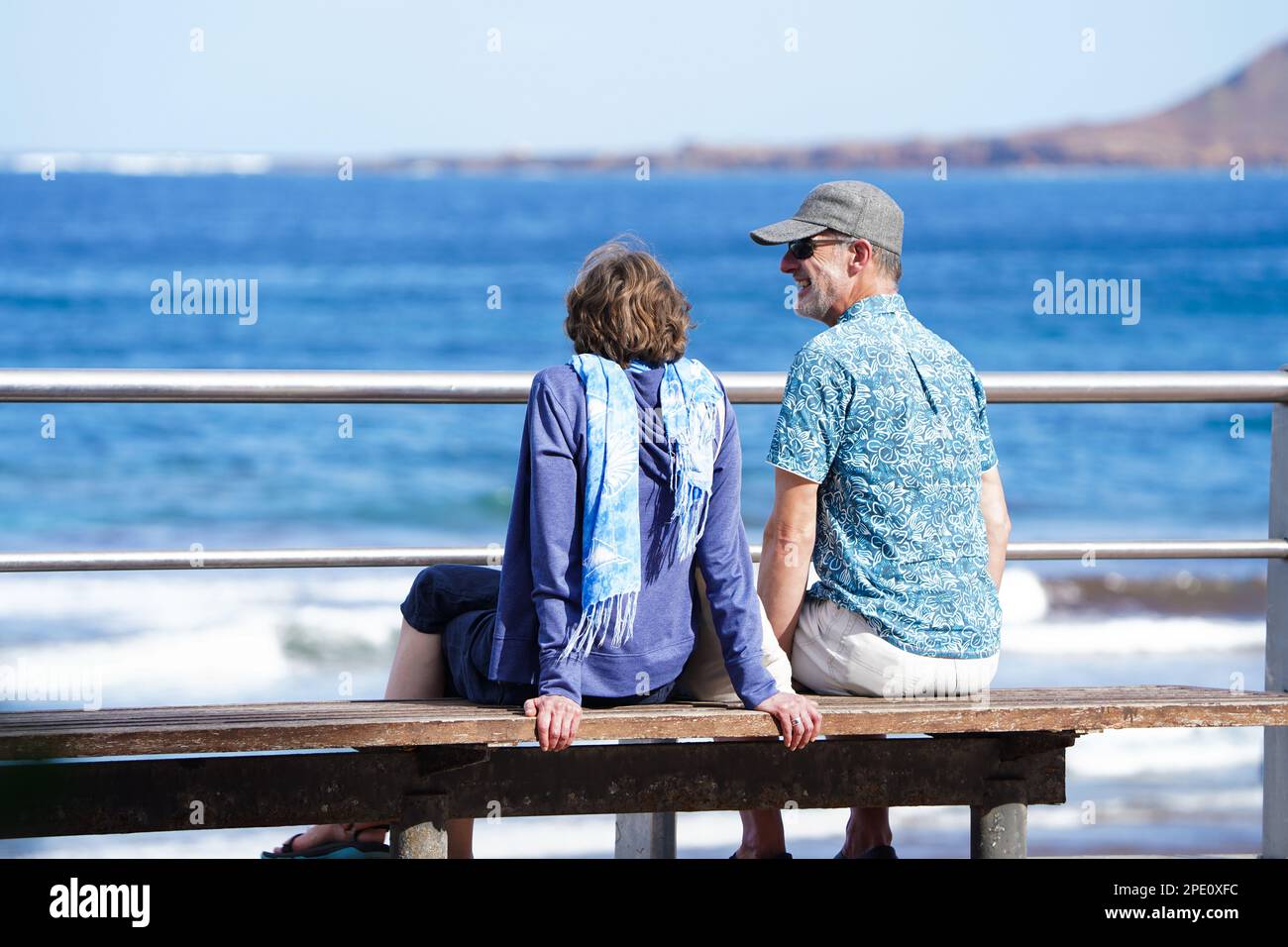 Couple of old retired seniors man and woman siting at a bench watching ocean by the beach and laughind or smiling Stock Photo