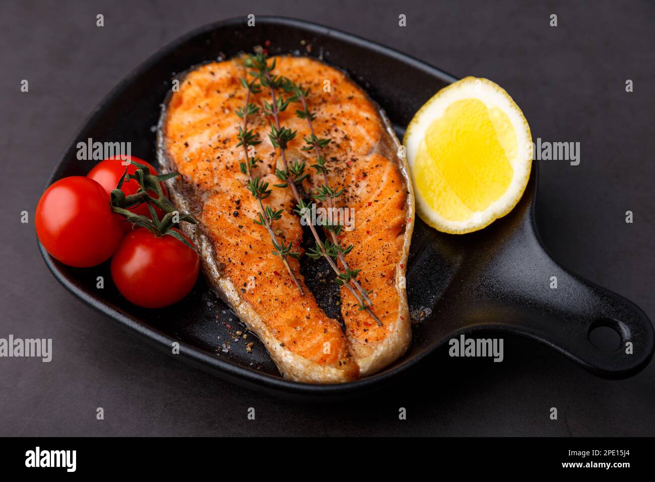 Grilled salmon with cherry tomatoes, thyme and lemon on a small black