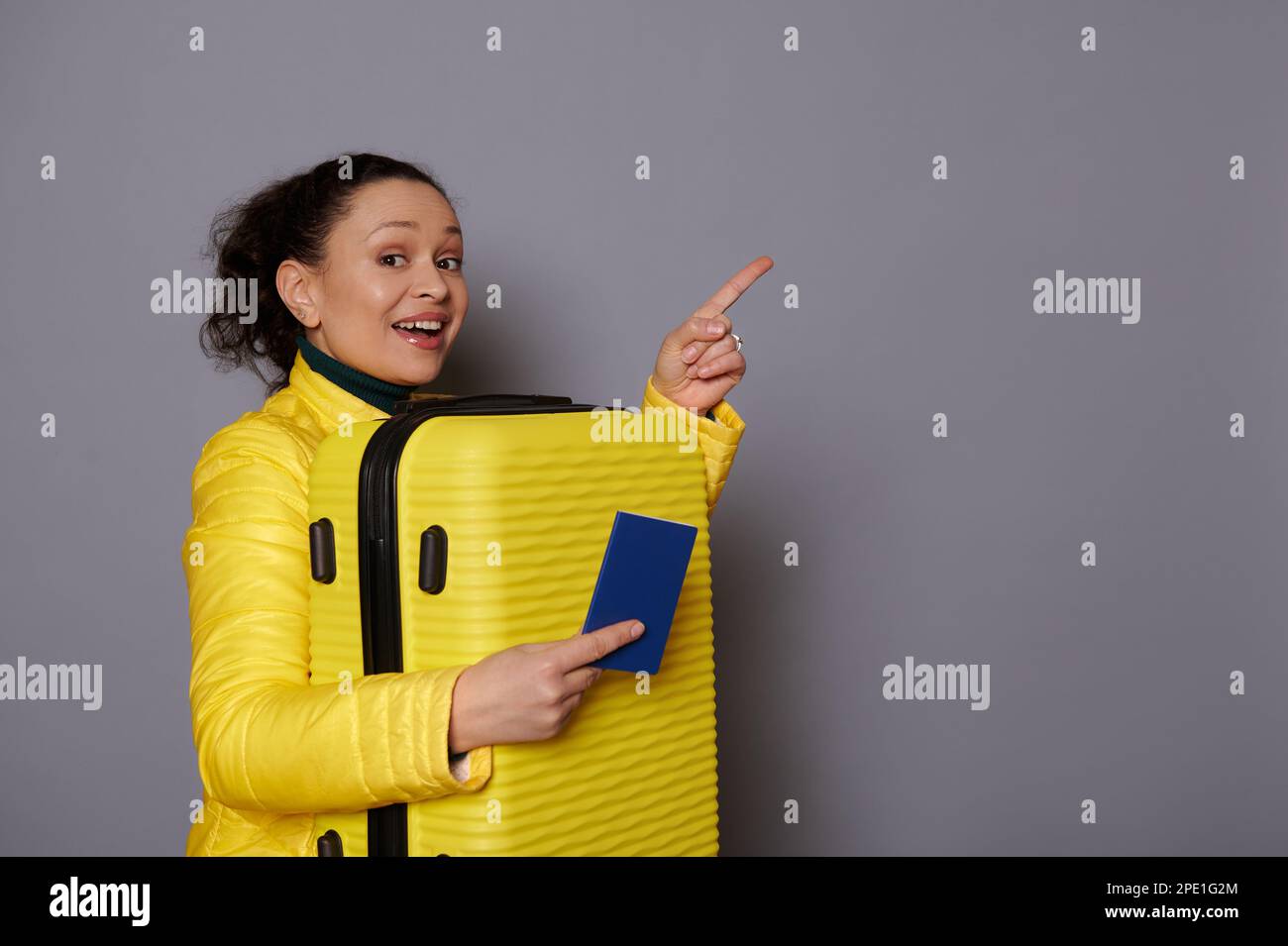 Attractive woman in yellow jacket, carrying her suitcase, pointing at