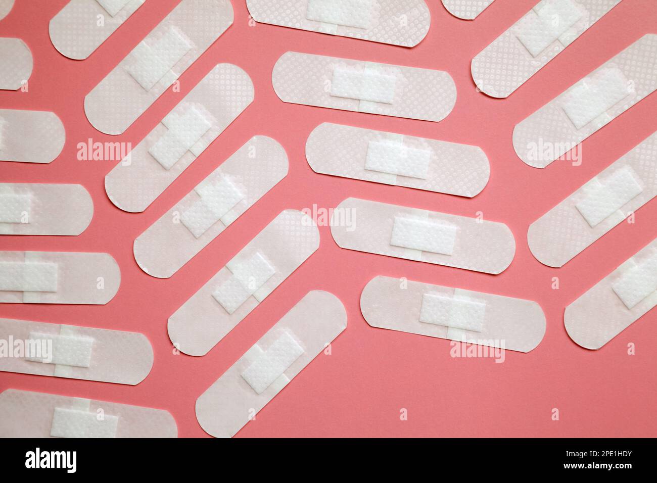 Many white adhesive band aids arranged on pink background. Transparent medical sticking plasters
