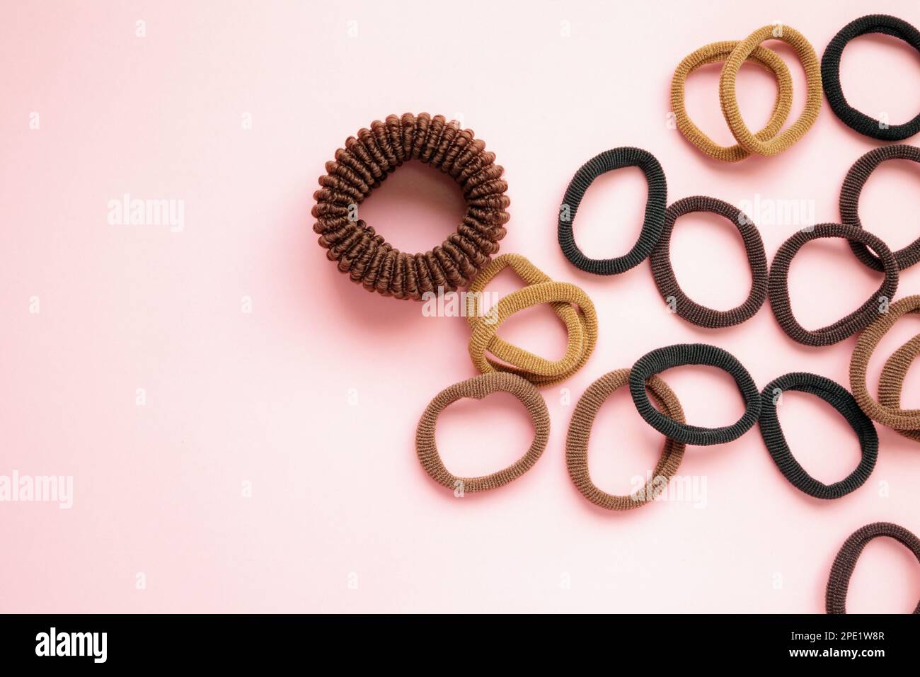 Many elastic hair ties of natural colors on a pink background with copy space. Black, brown, beige, black, thin and thick hair holders Stock Photo