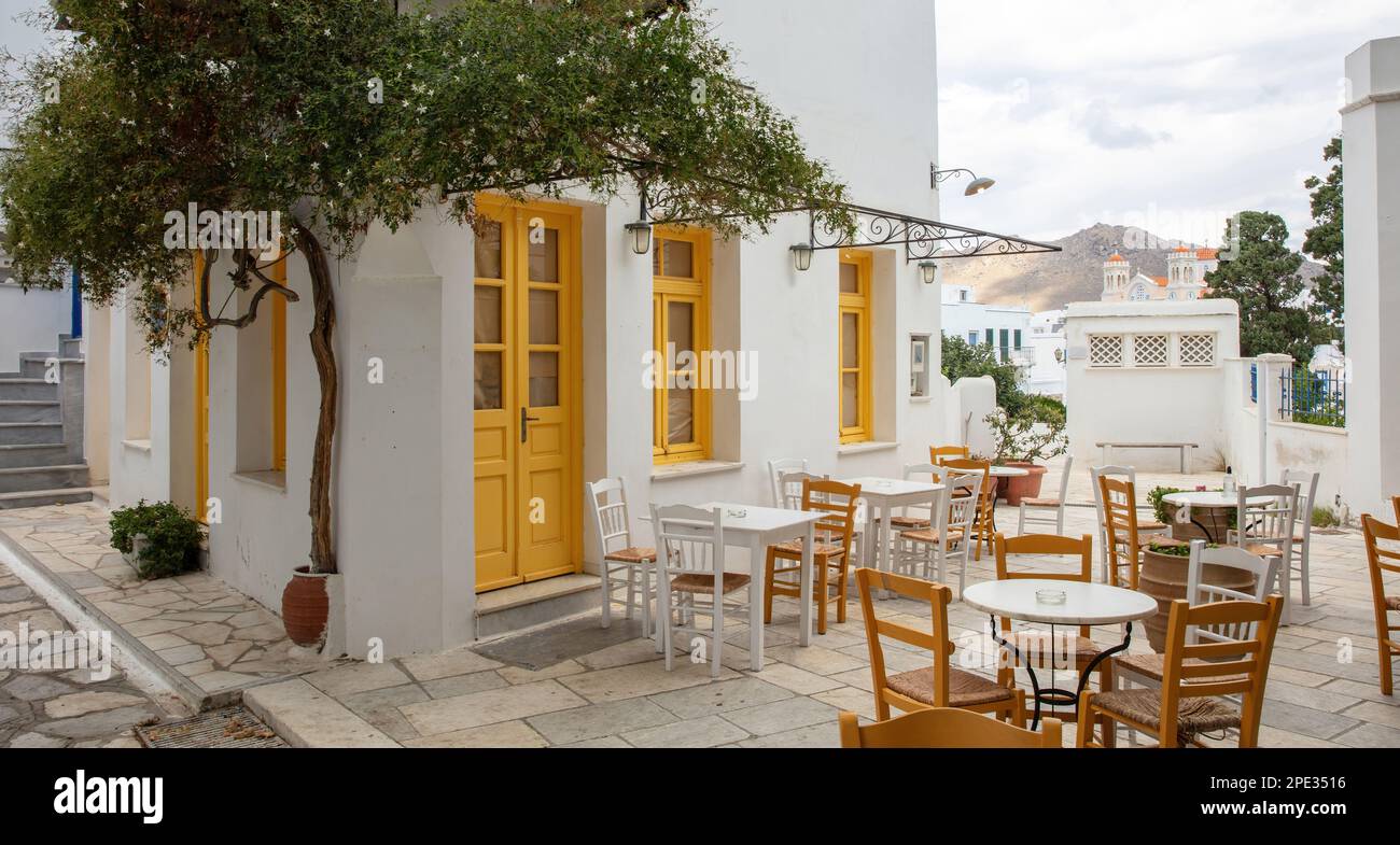 Greece. Tinos island Cyclades. Outdoors traditional cafe with yellow windows at Pyrgos village. Empty chair and table on paved yard Stock Photo