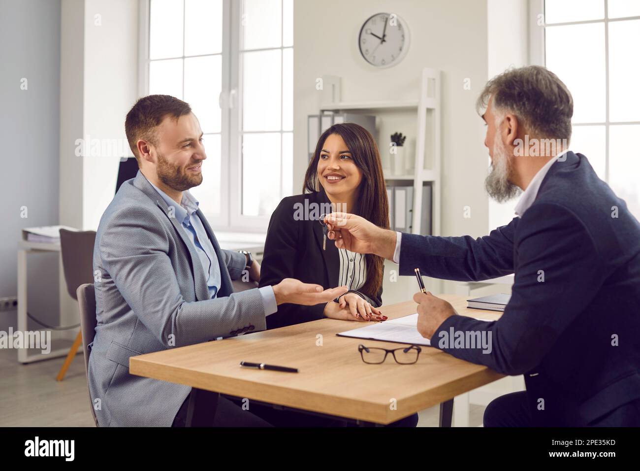 Man realtor with beard giving house key to a couple customers sitting in the office Stock Photo