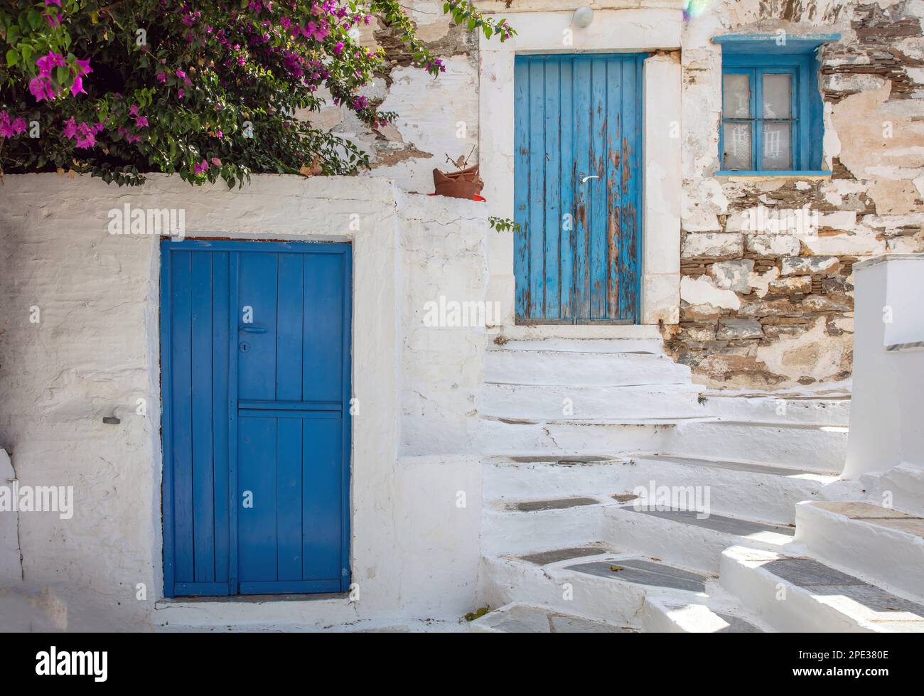 Greece. Tinos island of art, Cycladic architecture at Pyrgos village, bougainvillea on whitewashed wall, blue door and windows, sunny day. Stock Photo