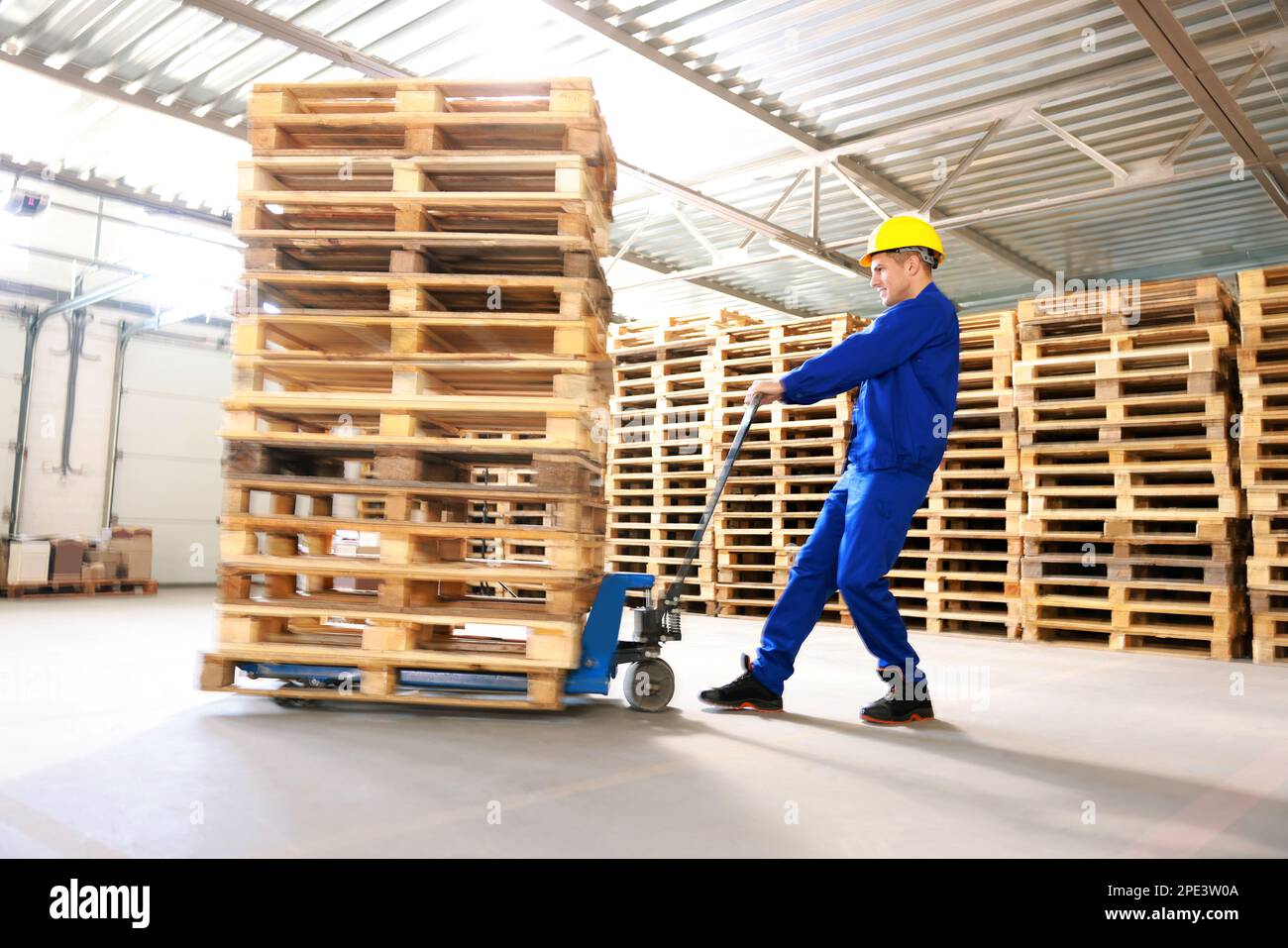 Worker moving wooden pallets with manual forklift in warehouse Stock ...