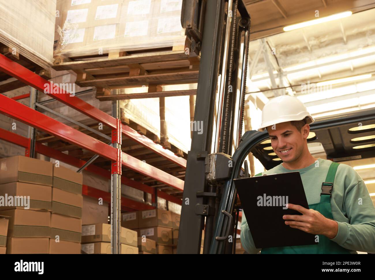 Worker near forklift truck with cardboard boxes in warehouse. Logistics ...