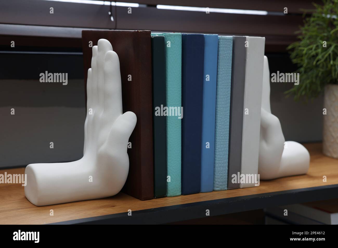 Beautiful hand shaped bookends with books on shelf indoors Stock Photo