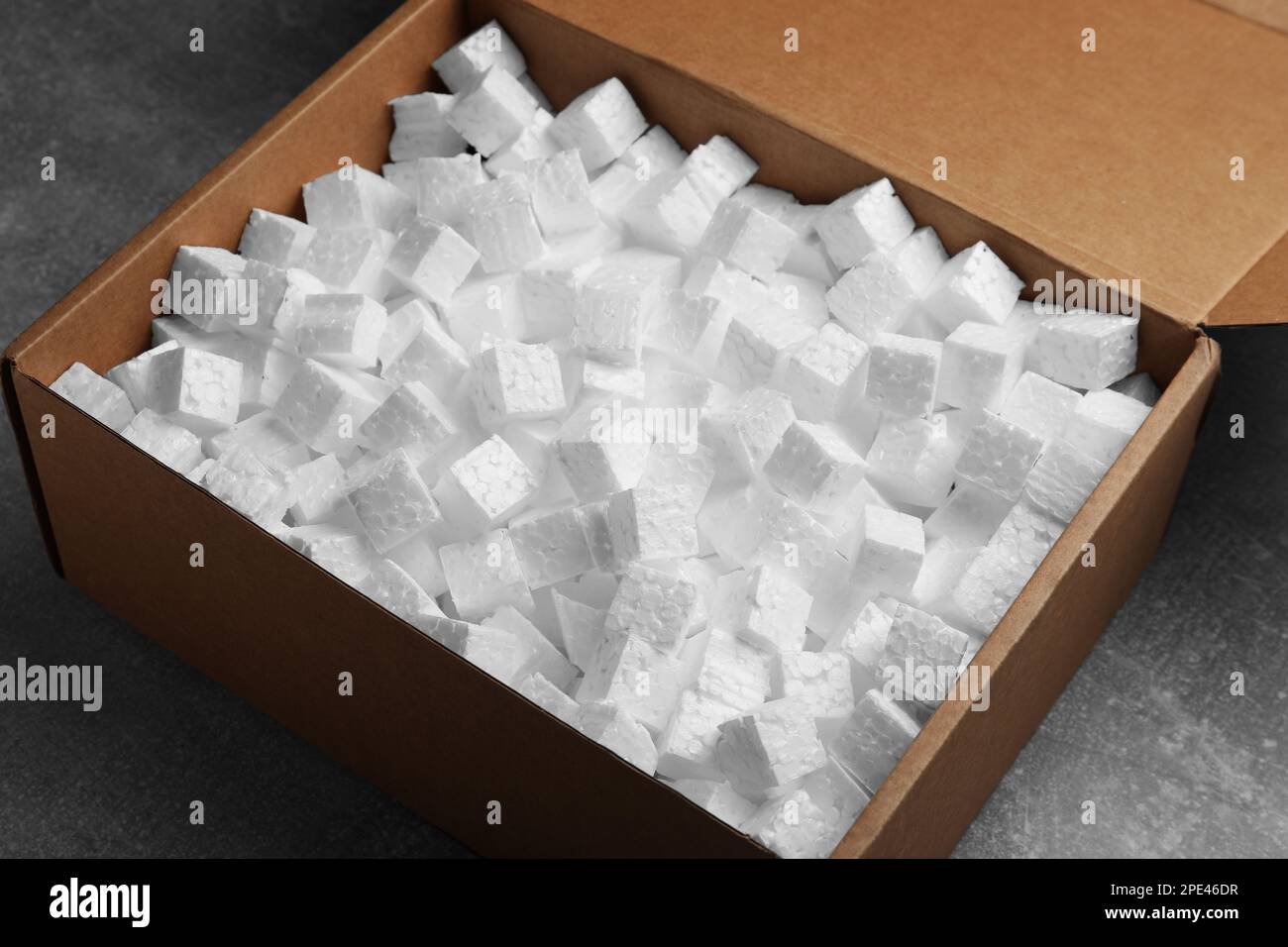 Cardboard box filled with polystyrene styrofoam pieces on grey table