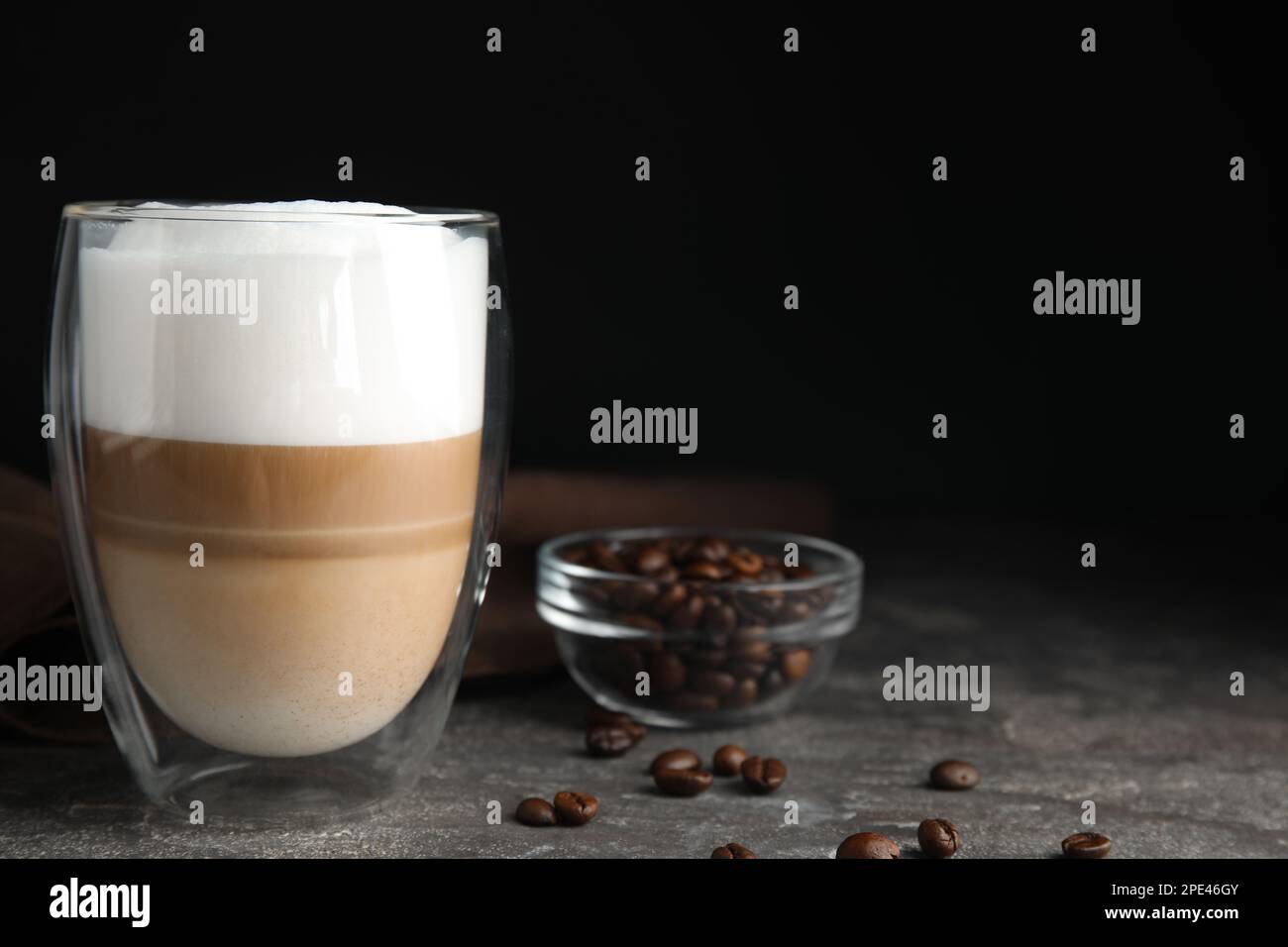 Delicious latte macchiato and coffee beans on grey table, space for