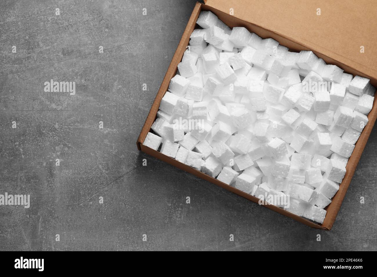 Cardboard box filled with polystyrene styrofoam pieces on grey