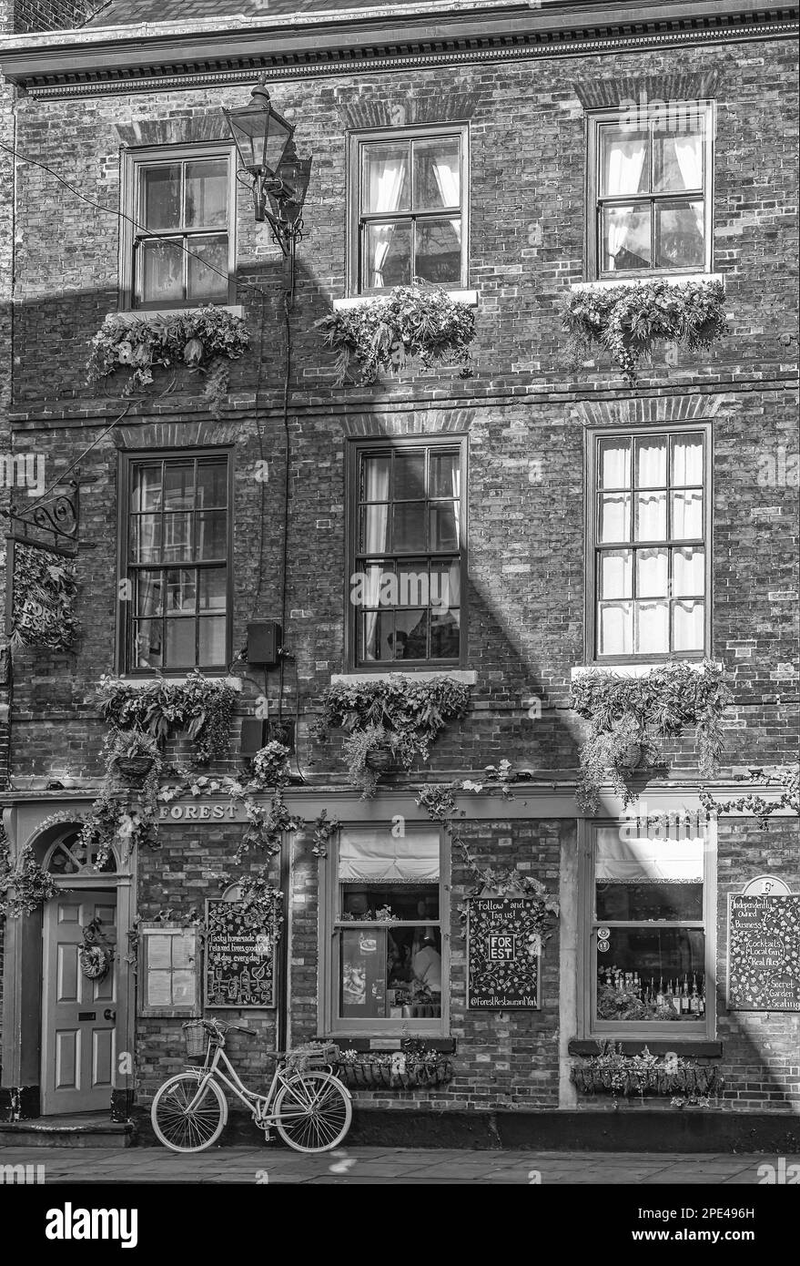 A brick built hotel and restaurant caught in a winter sun. Foliage hangs down from window boxes and a bicycle leans against the wall. A diagonal shado Stock Photo