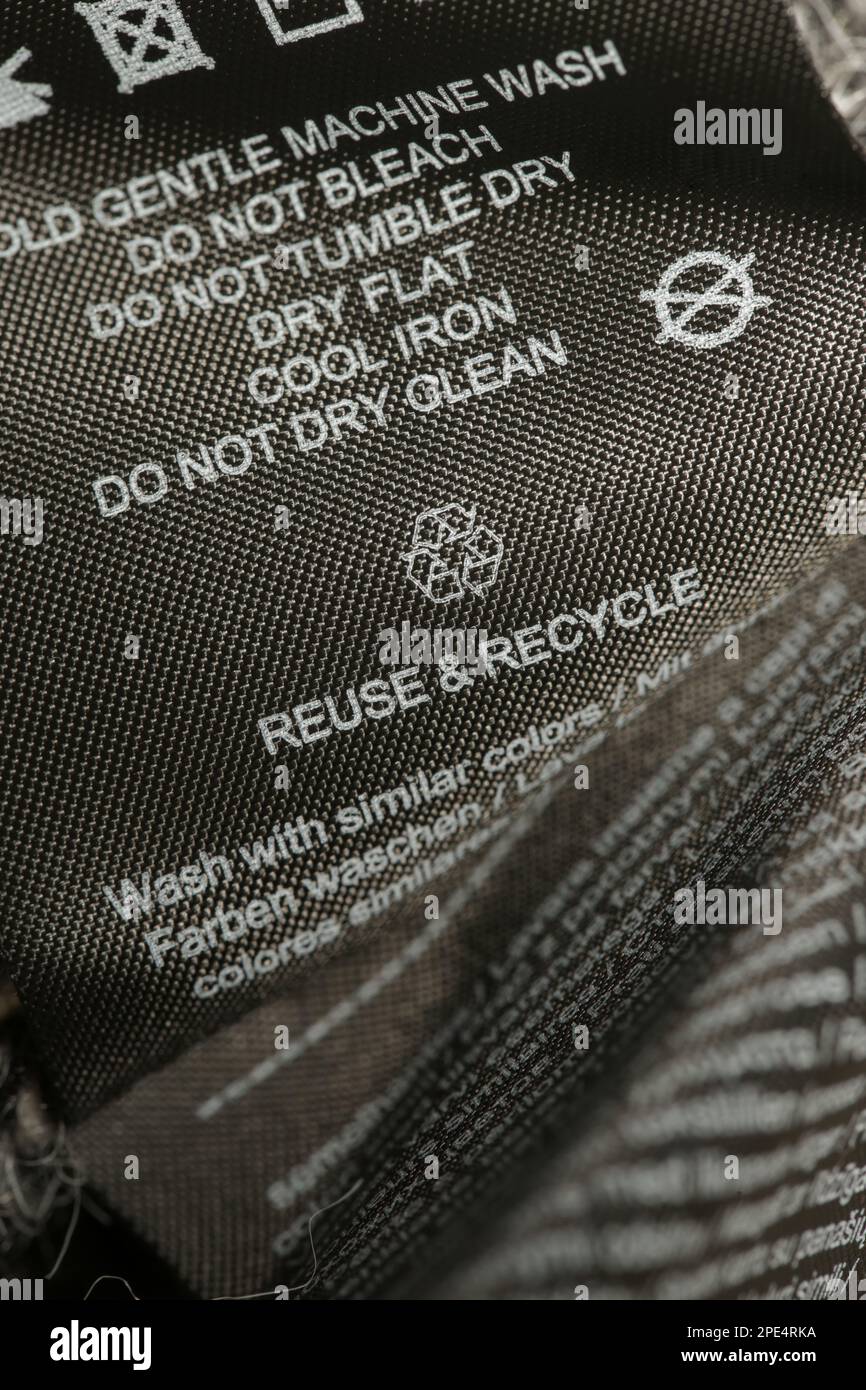 Fabric composition label, Washing instructions and recycling sign on black fabric label. Laundry tag on clothes. Stock Photo