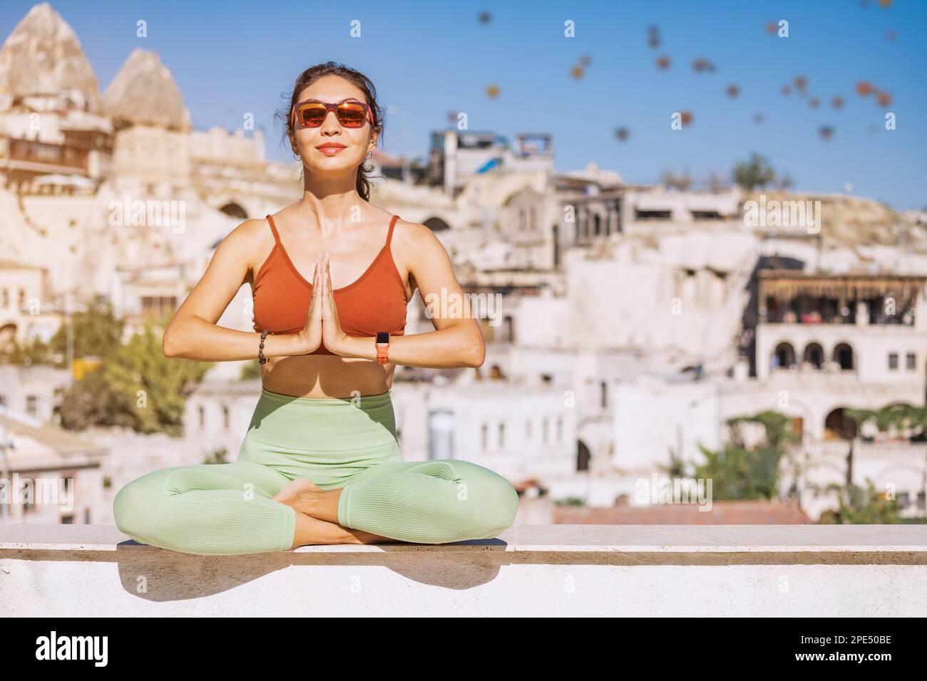 Happy girl does yoga exercises and meditation in Cappadocia, Turkey, with hot air balloons flying in the background Stock Photo