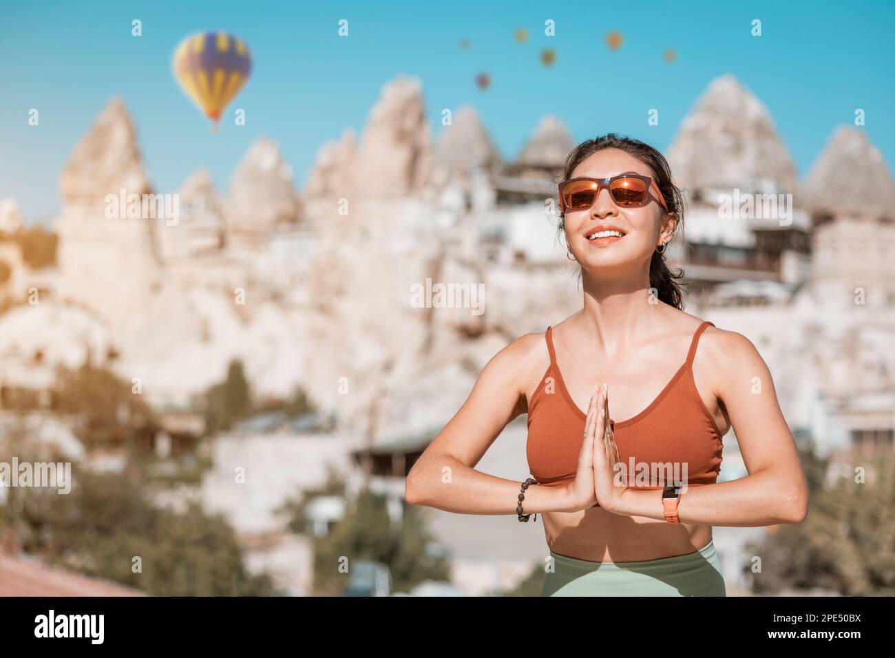 Happy girl does yoga exercises and meditation in Cappadocia, Turkey, with hot air balloons flying in the background Stock Photo