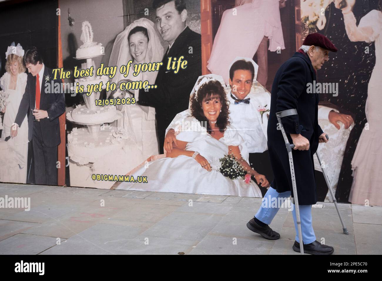 A disabled man walks with the help of crutches past a retail hoarding featuring a young bride and groom couple celebrating their wedding day, a picture of loyalty, dedication from youth to pension age, on 13th March 2023, in London, England. Stock Photo