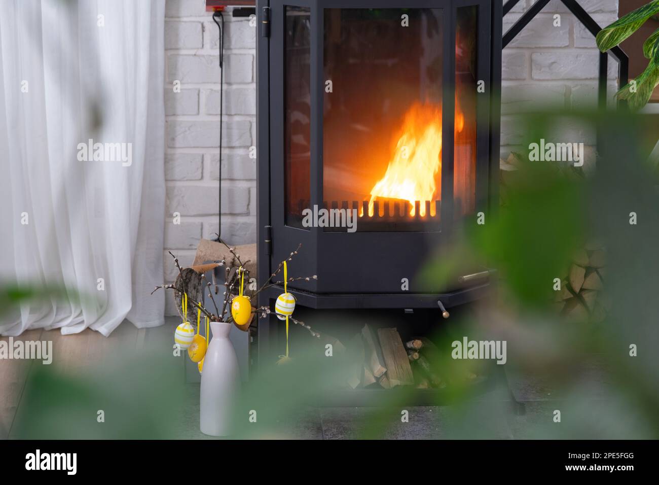 Easter decor near fireplace stove with fire and firewood. Cozy home