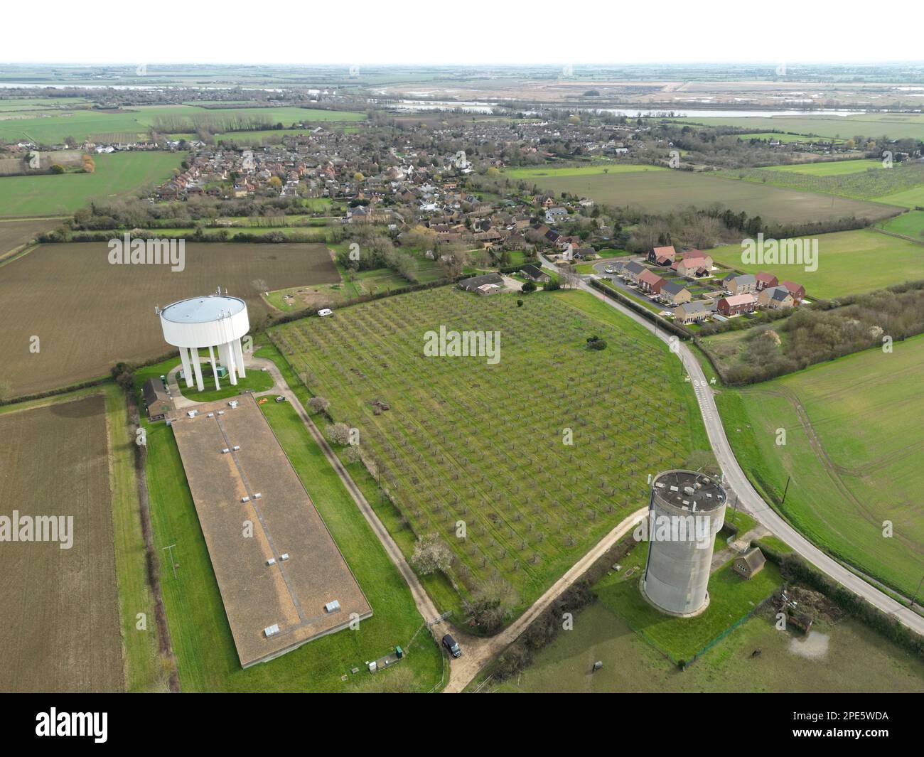 Drone view of a large concrete water tower on the left seen next to a huge chicken shed. A nearly 5G array is seen on a grey water tower. Stock Photo