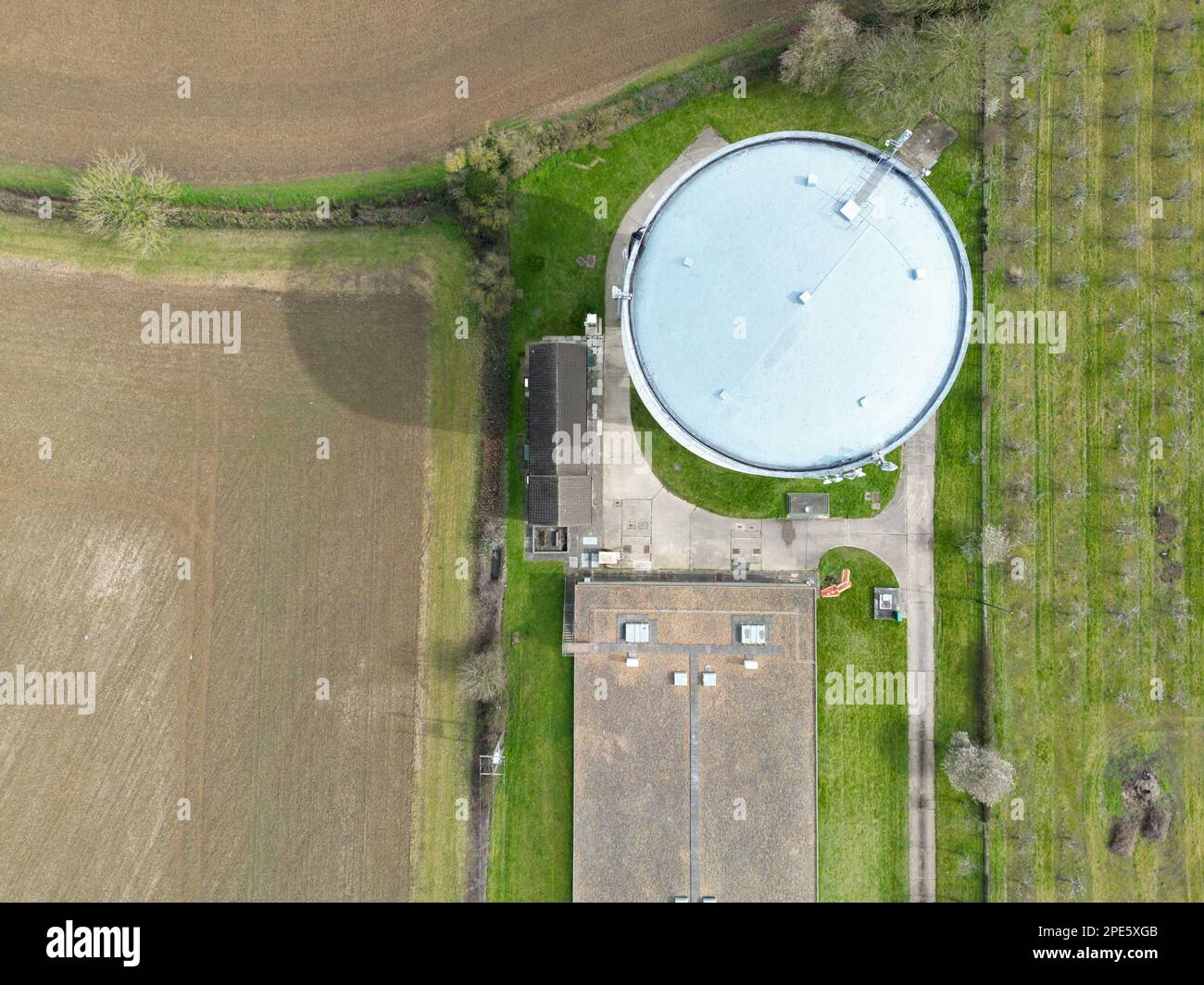 Aerial, top down view of a large water tower seen at the edge of a large shed which houses chickens. Stock Photo