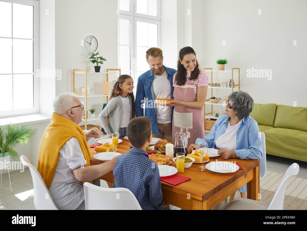 Dinner in big family at table in living room, mom holding a pie and looking at grandma with smile. Stock Photo